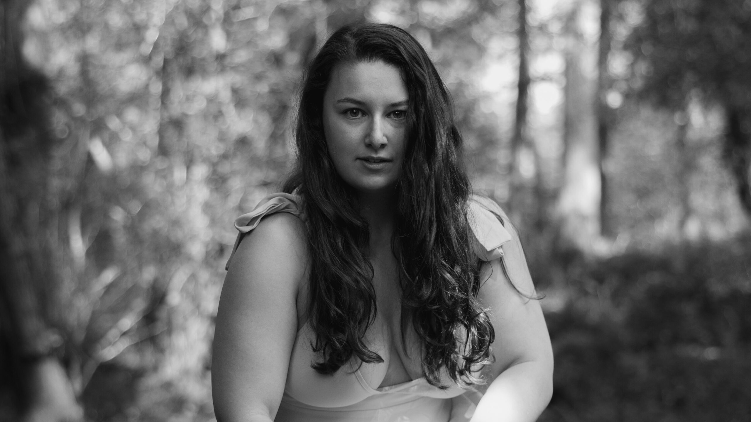 A black and white image of a woman with long dark hair stares primally into the camera