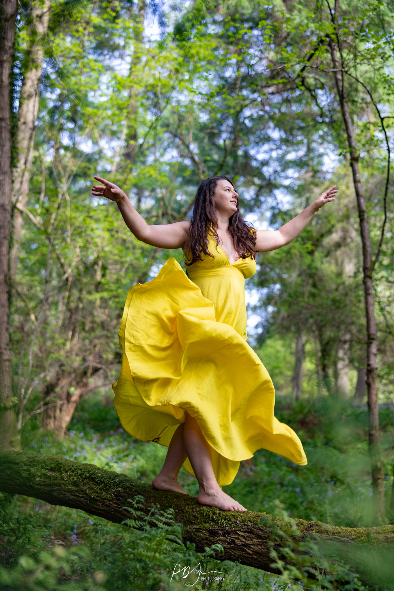 Woman in a pink dress and hiking boots standing on a log in the forest