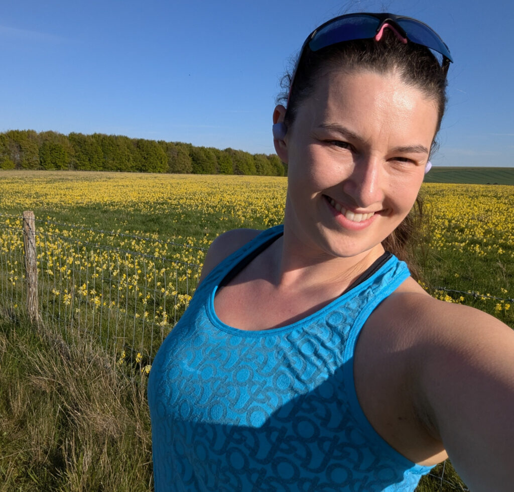 A woman wearing a blue exercise top takes a selfie in front of a vast field of yellow cowslips