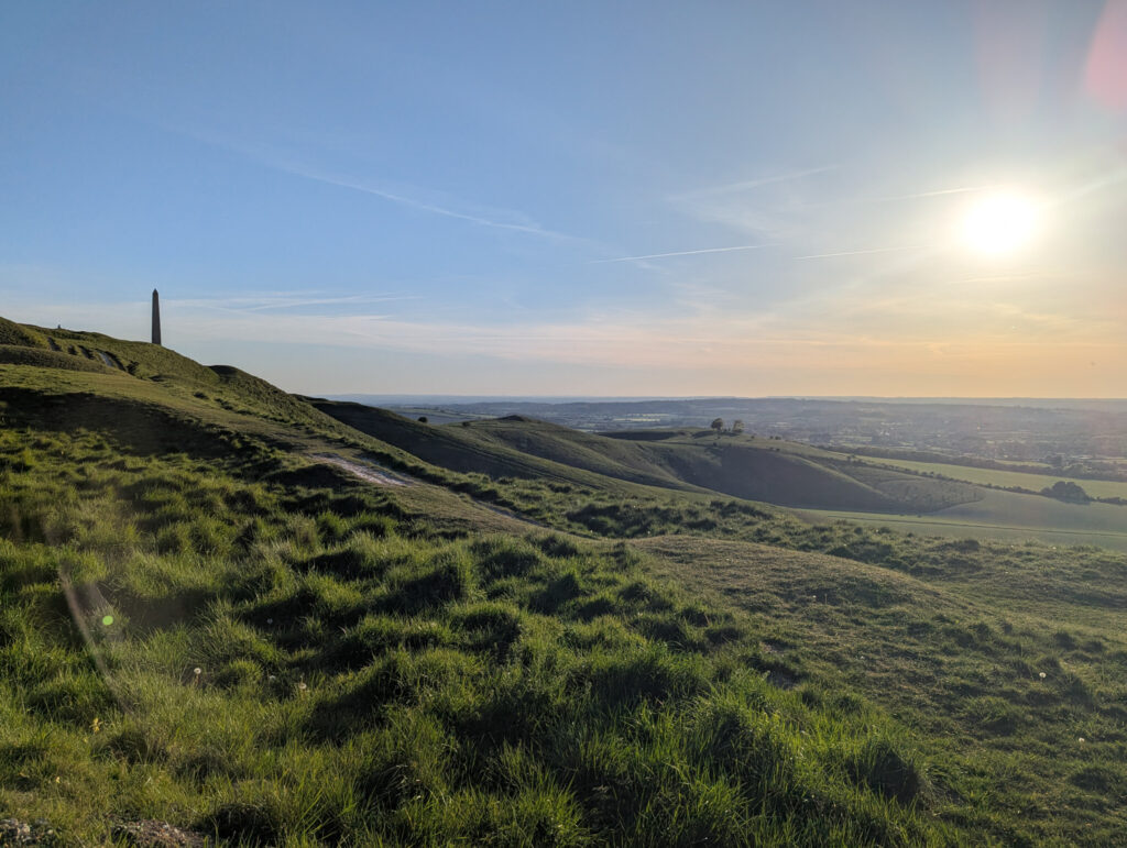 An obelisk monument stands on a hill, with the English countryside spreading out behind it