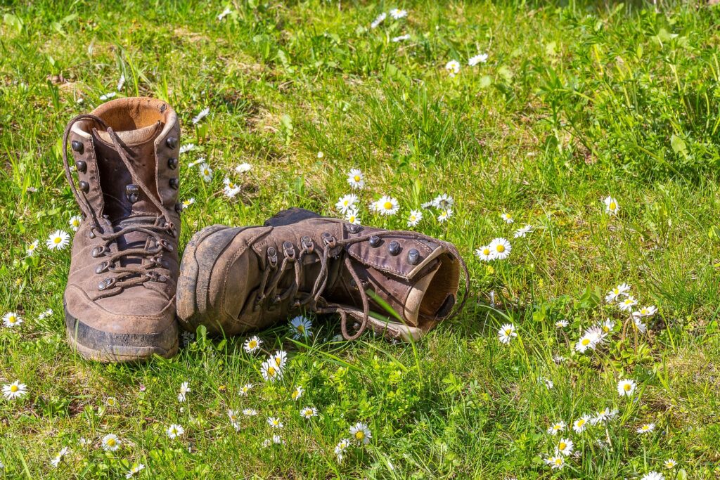 A pair of empty brown hiking boots in a grass field full of white daisies